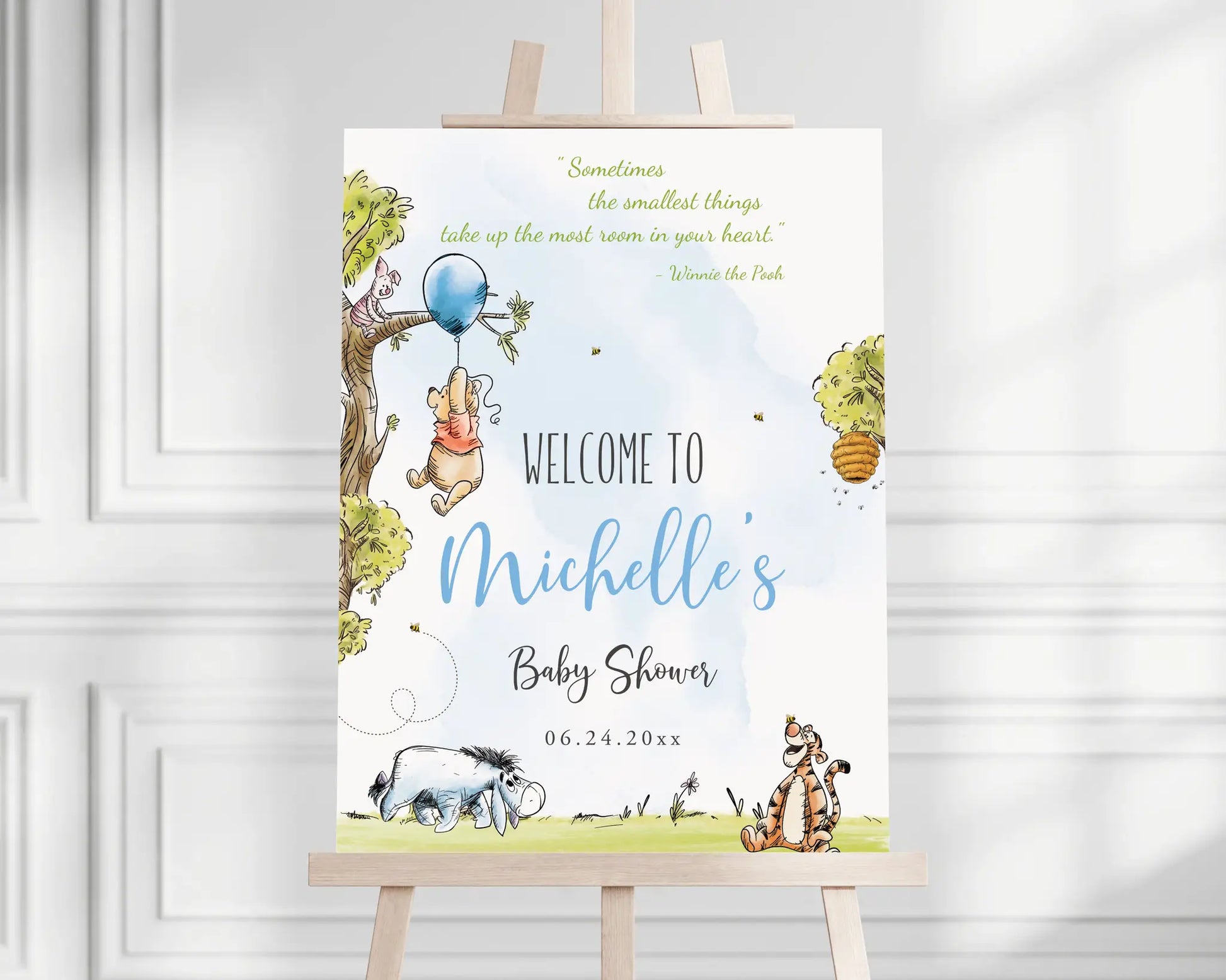 Winnie the Pooh baby shower welcome sign with blue balloon and woodland tree displayed on an easel, printable Canva template.